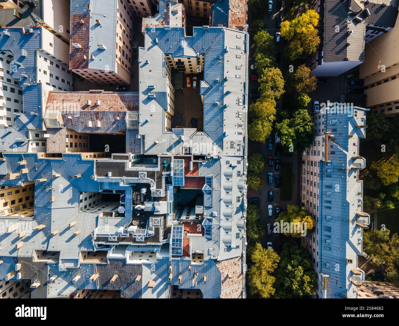 Area urbana molto trafficata con edifici interconnessi, tetti blu grigi, cortili interni, strade strette e una strada alberata sulla destra. Foto Stock