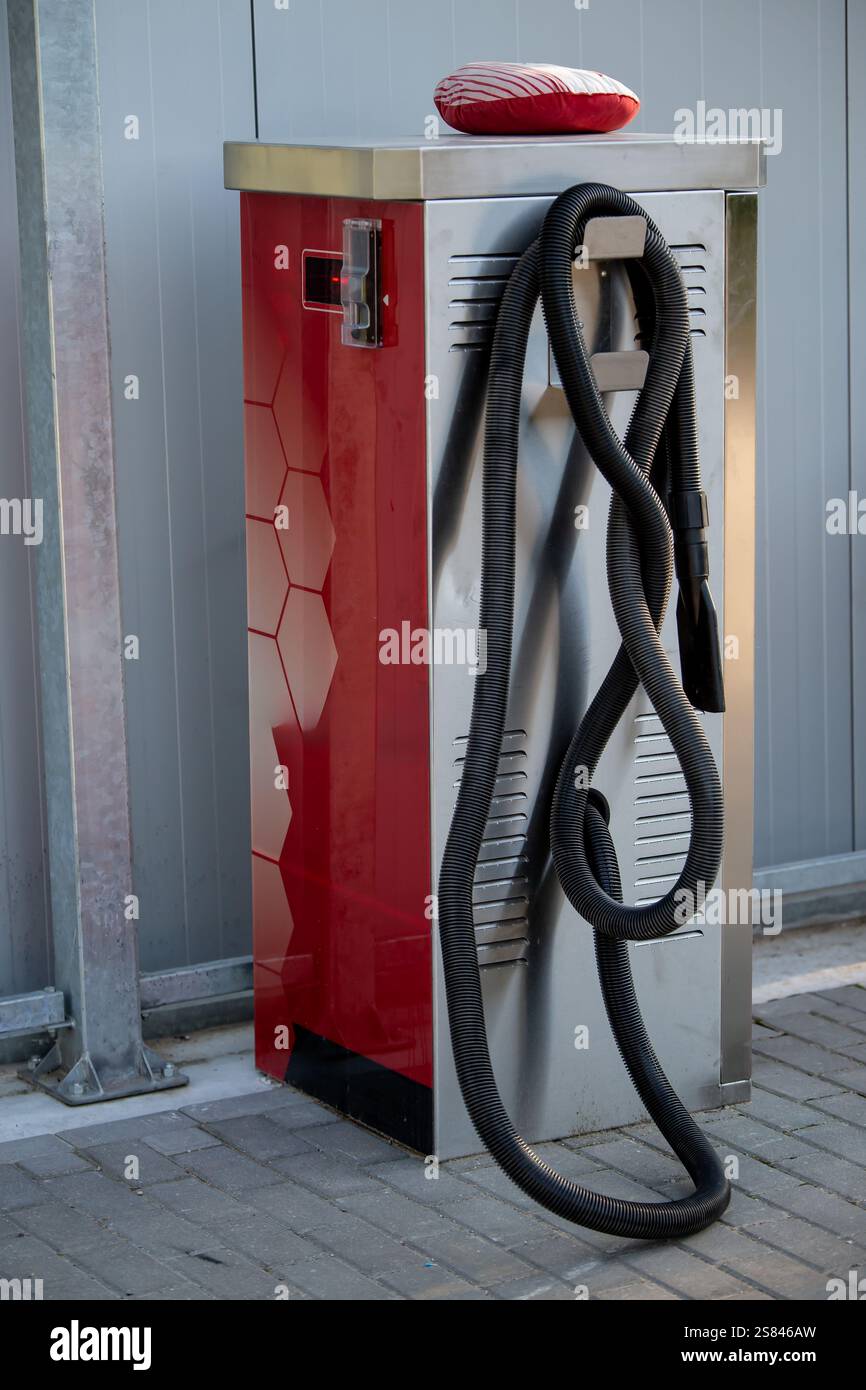 Base per aspirapolvere rossa e argento con motivo esagonale, tubo nero a spirale e tampone per la pulizia sulla parte superiore, posizionata su una superficie pavimentata vicino a una parete grigia. Foto Stock