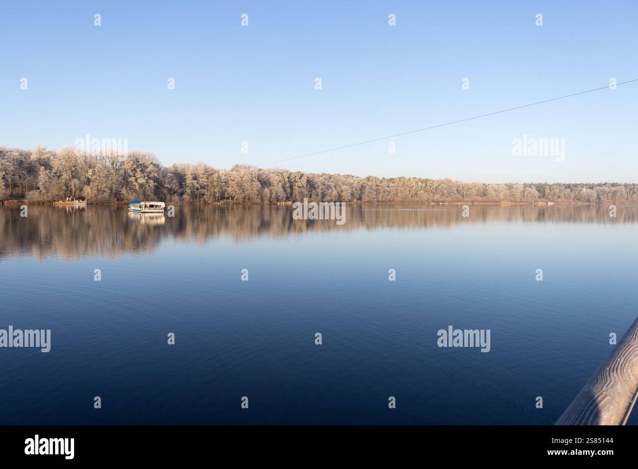 Una tranquilla mattinata invernale a Straussee, con una barca che galleggia sull'acqua ferma e alberi ricoperti di gelo che si riflettono nel lago sotto un cielo azzurro. Foto Stock