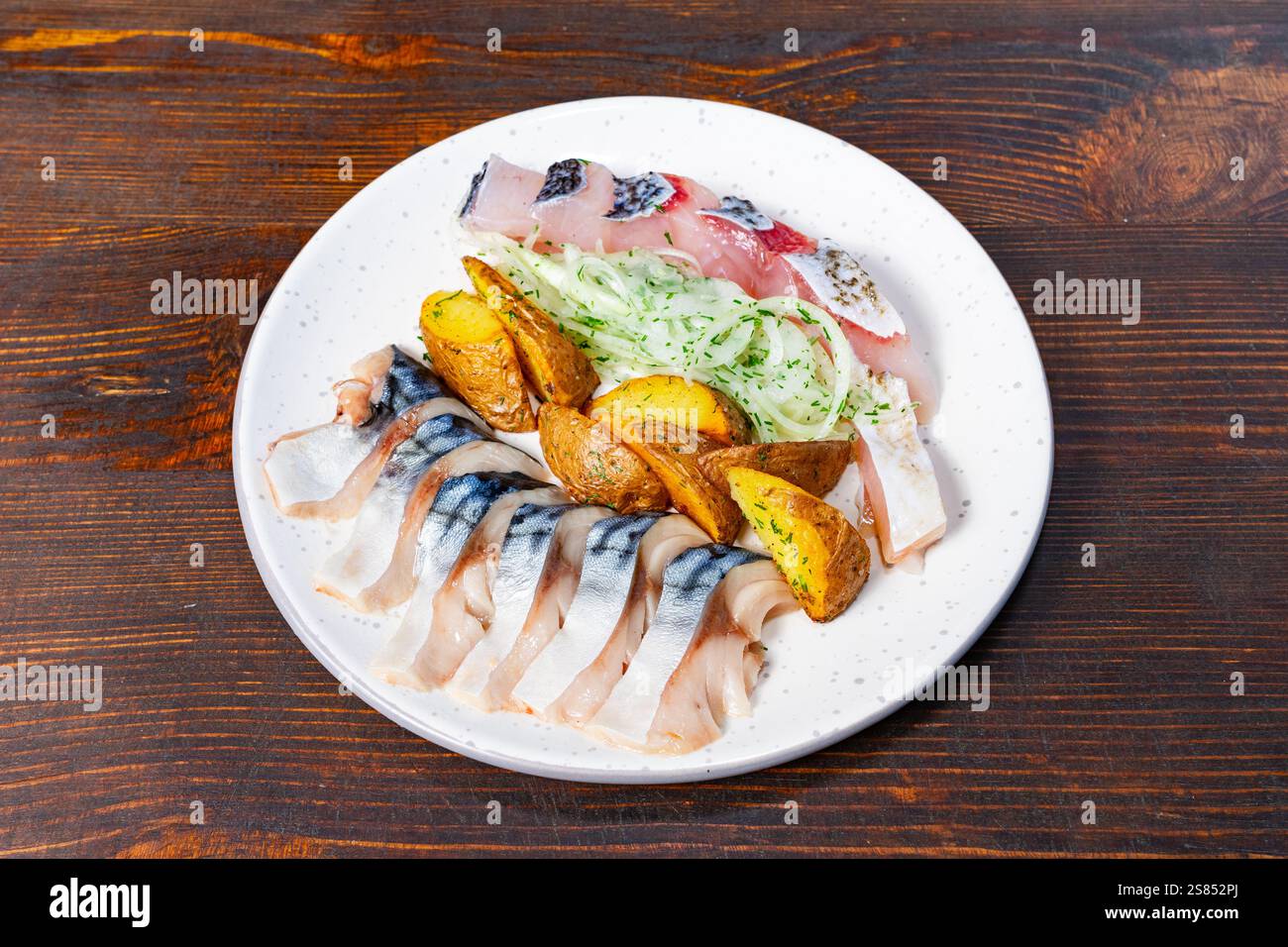 Un piatto di pesce splendidamente organizzato presenta vari tipi di pesce fresco, accompagnato da spicchi di patate arrosto e un lato di insalata croccante. Perfetto f Foto Stock
