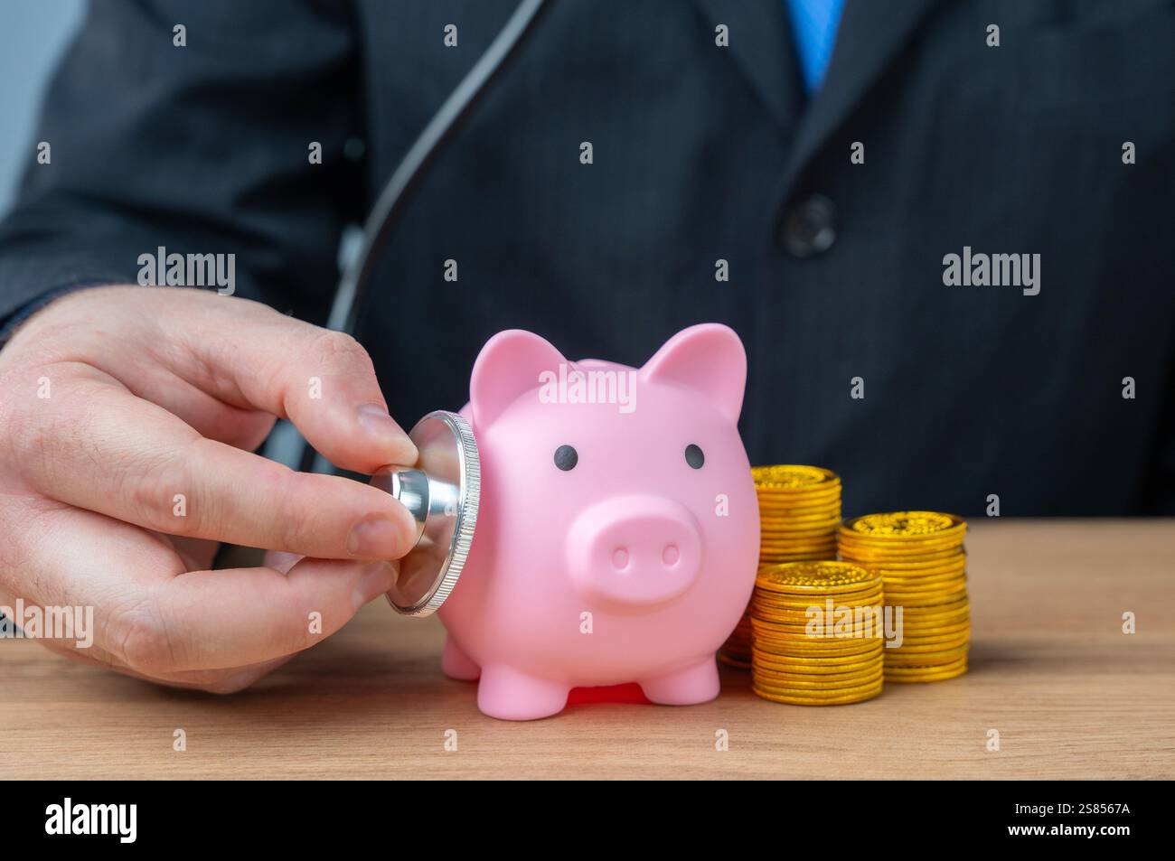 L'uomo d'affari ascolta il maialino con uno stetoscopio. Salute finanziaria. Liquidità delle attività. Sicurezza economica. Gestione contabile. Foto Stock