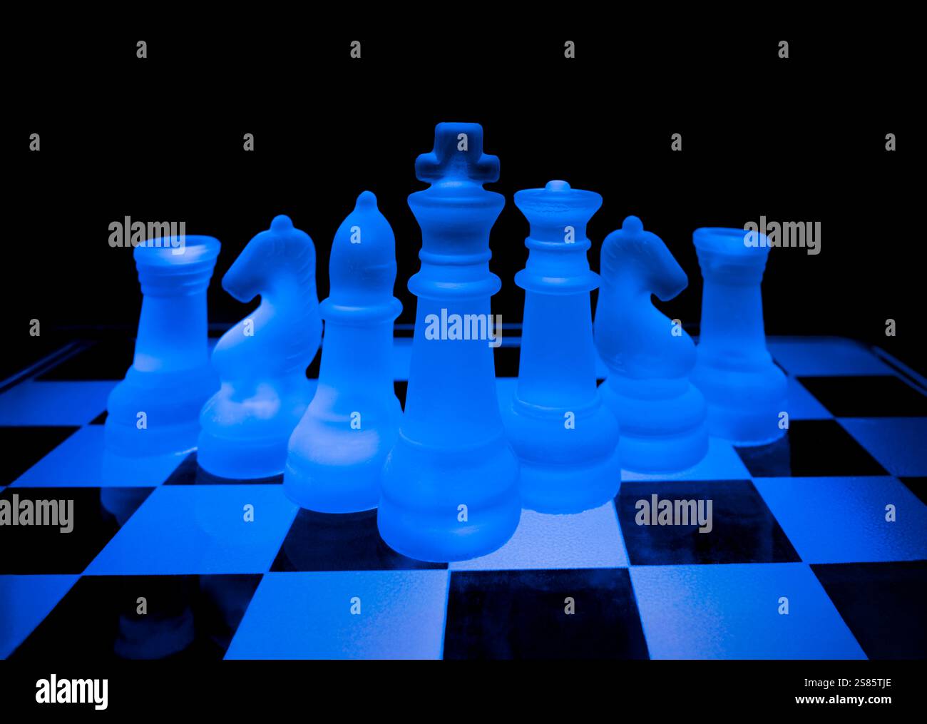 Scacchi in vetro traslucido disposti su una scacchiera traslucida e illuminati con luci colorate Foto Stock
