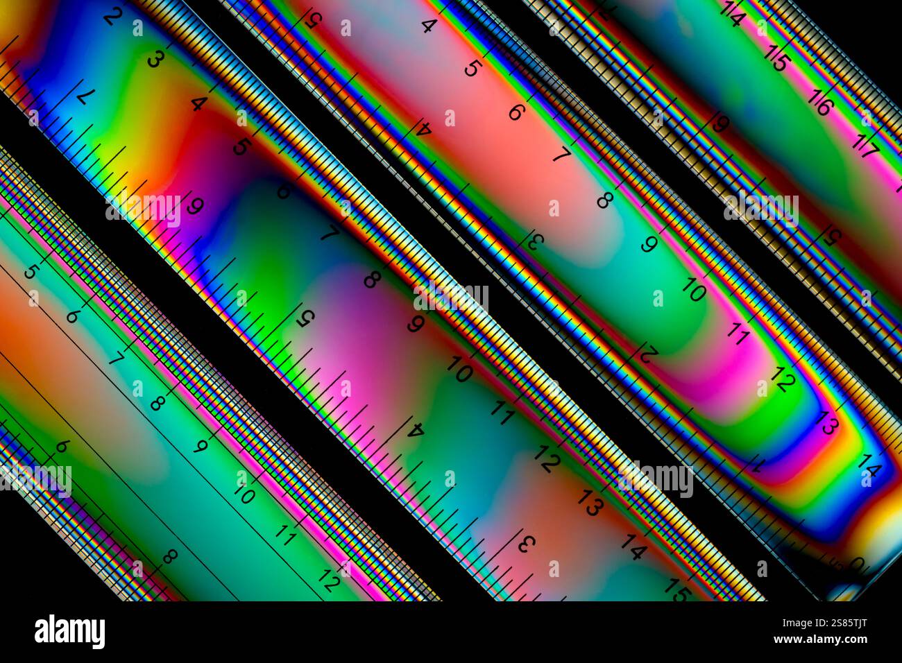 Quattro righelli in plastica di un set di geometria, fotografati con luce a polarizzazione incrociata, che mostrano una gamma di colori Foto Stock