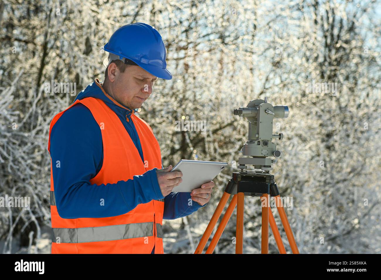 Surveyor che utilizza tablet e teodolite durante l'inverno topografia in un paesaggio innevato. Foto Stock