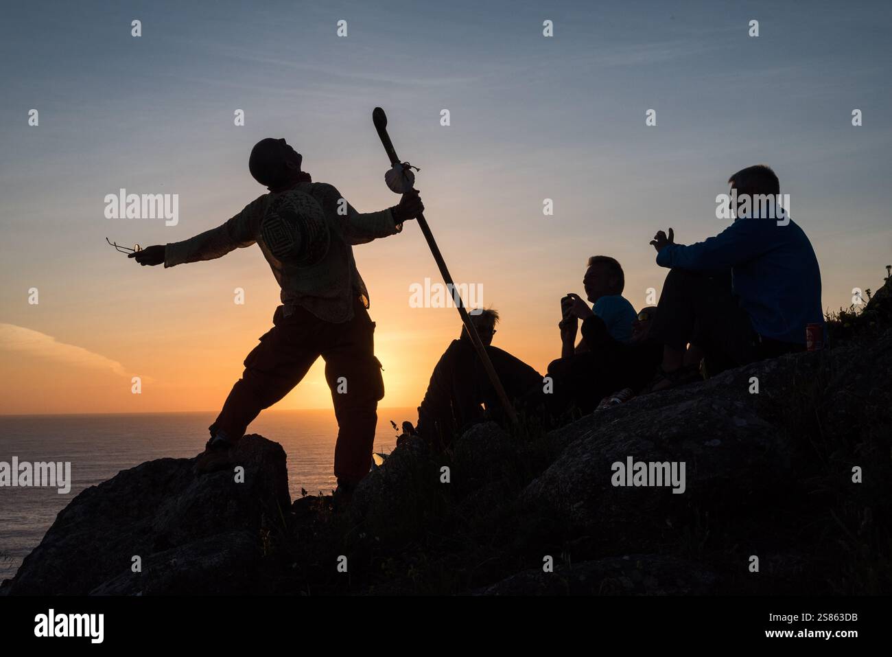 Pellegrini sul Capo Finisterre, che segna la fine del Camino de Santiago in Spagna. Silhouette di un uomo sulle rocce con un bastone da passeggio, parlando wi Foto Stock