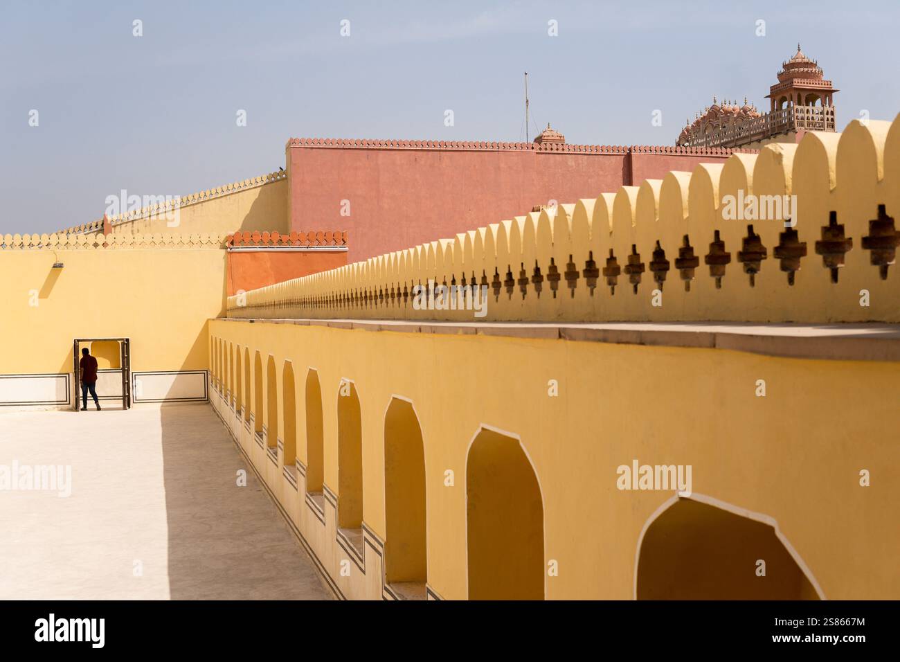 Uomo silhouette che cammina nel cortile del palazzo Hawa Mahal a Jaipur, India. Turista europeo alla scoperta dell'architettura del Rajasthani nelle calde giornate di sole Foto Stock