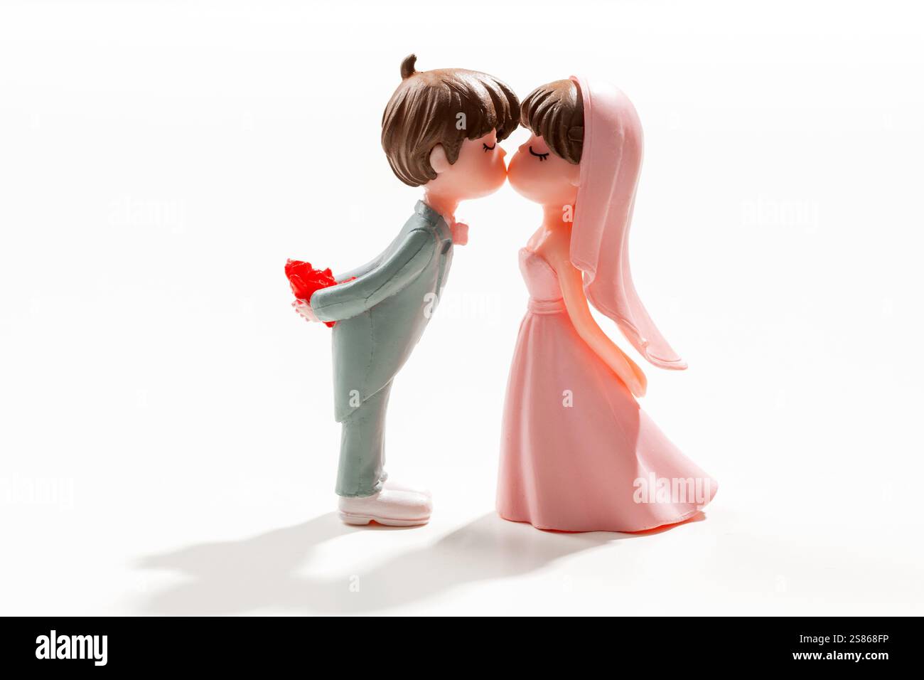 Statuette di sposo e sposa che si baciano, celebrano il loro matrimonio, isolate su sfondo bianco Foto Stock