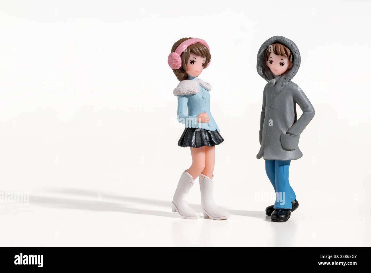 Statuette di giovane uomo e donna che indossano abiti invernali in piedi su uno sfondo bianco Foto Stock
