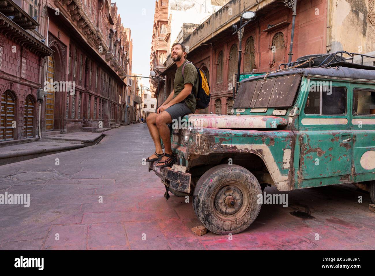 Turista maschile seduto sul cofano di una vecchia ira di un'auto a Bikaner, Rajasthan, India Foto Stock
