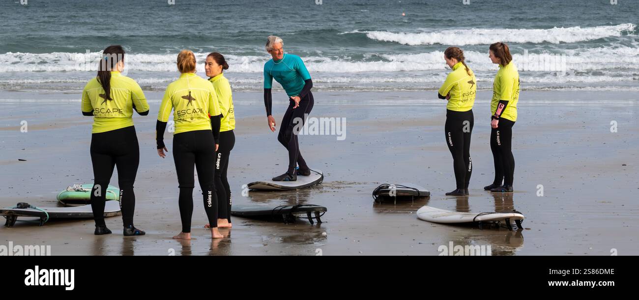 Un'immagine panoramica di un istruttore di surf della Escape Surfing School che tiene una lezione di surf con un gruppo di studentesse a Towan Beach a ne Foto Stock