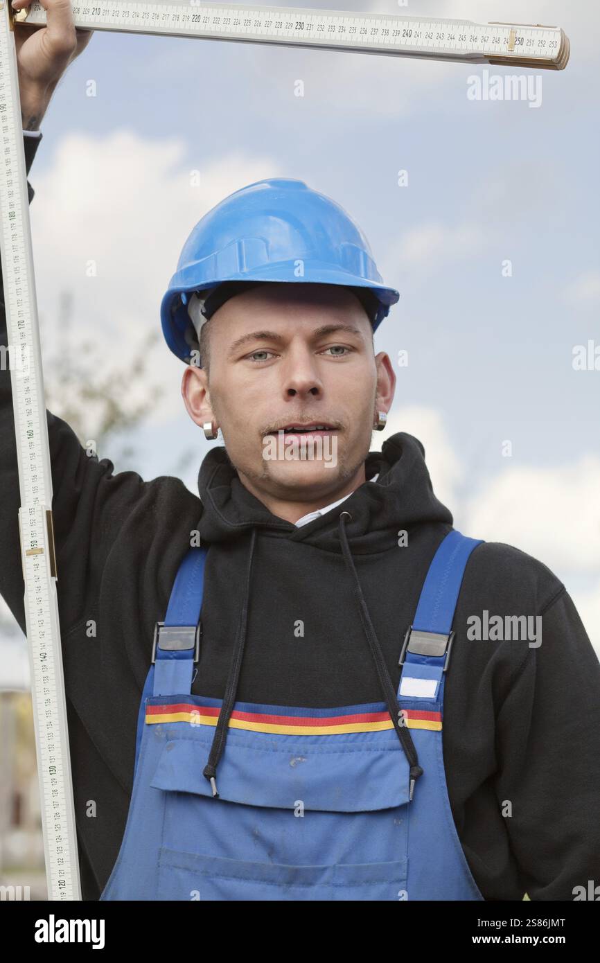 Il lavoratore manuale in elmetto si trova all'aperto con righello pieghevole, Germania, Europa Foto Stock
