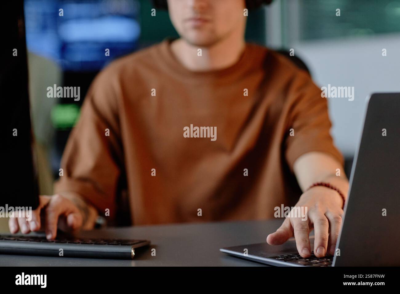 Immagine ritagliata di un programmatore maschio irriconoscibile che utilizza la codifica di computer e laptop su più schermi mentre lavora nell'ufficio dell'azienda IT, spazio di copia Foto Stock