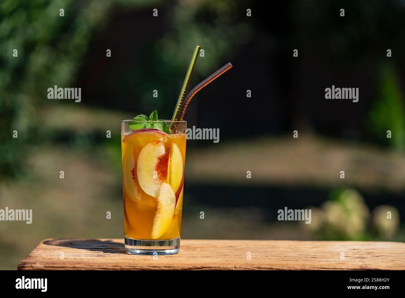 Un bicchiere di cocktail estivo o tè freddo con fette di pesca, ghiaccio e menta sullo sfondo naturale. Primo piano Foto Stock