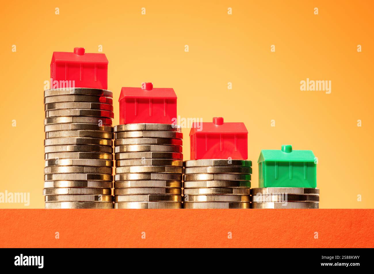 Concetto di calo dei prezzi immobiliari. Case su pile di soldi in pendenza. Foto Stock