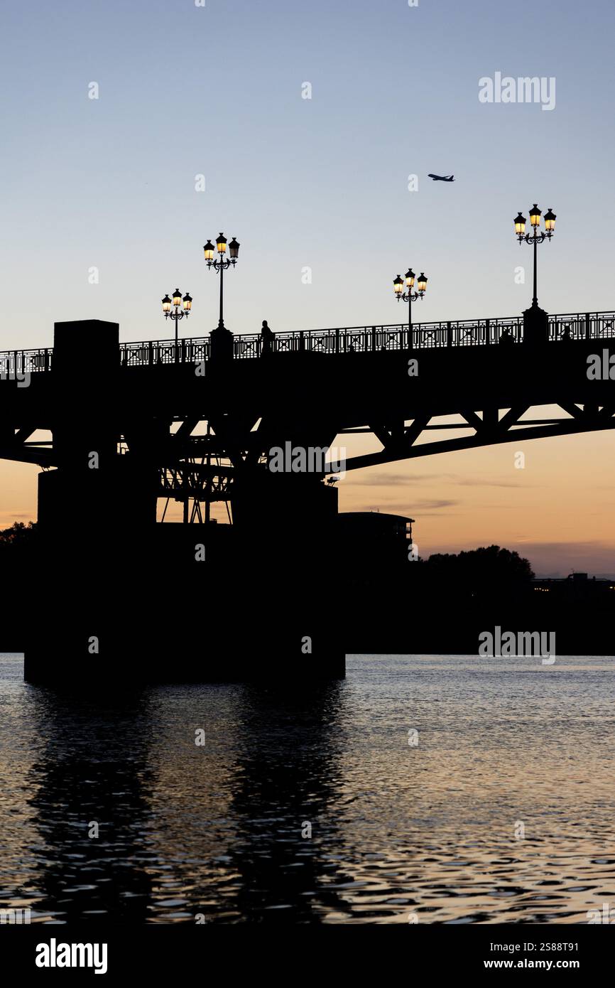 Silhouette panoramica di un aereo e ponte Pont Saint-Pierre a Tolosa, in Francia, catturata al tramonto. Eleganti lampioni illuminano la struttura. Foto Stock