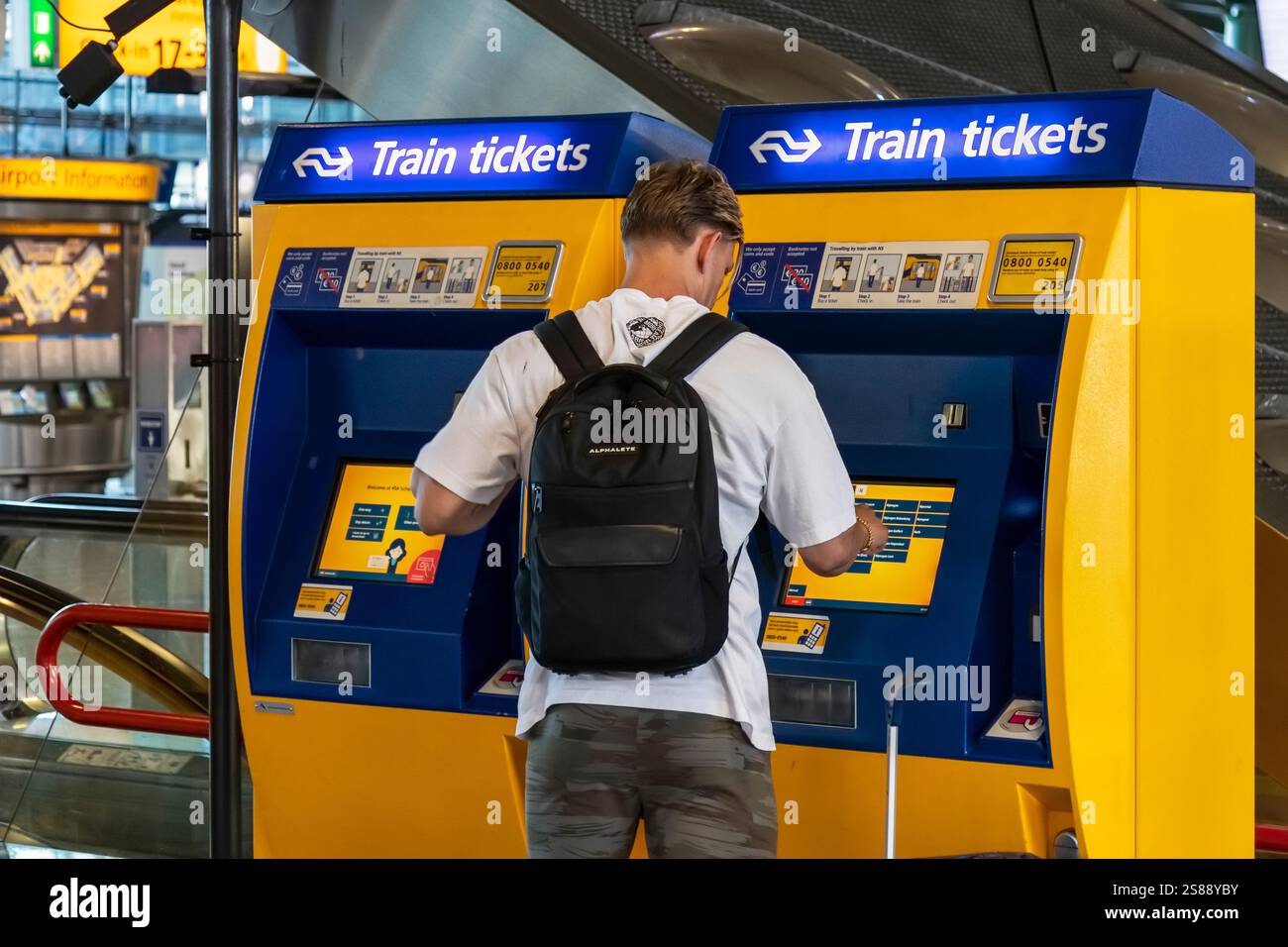 Un giovane con uno zaino acquista un biglietto del treno da una macchina nella hall dell'aeroporto internazionale Schiphol di Amsterdam. Foto Stock
