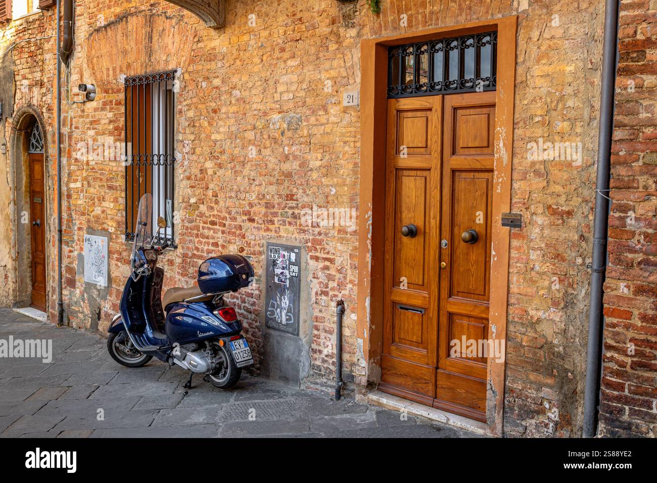 Una Vespa nera parcheggiata fuori da un appartamento con una grande porta di legno su una strada a Siena, in Italia Foto Stock
