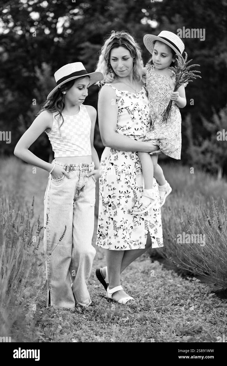 Una foto in bianco e nero di una donna e delle sue due figlie che camminano attraverso un campo di lavanda. Indossano abiti e cappelli estivi, godendosi la tranquillità Foto Stock