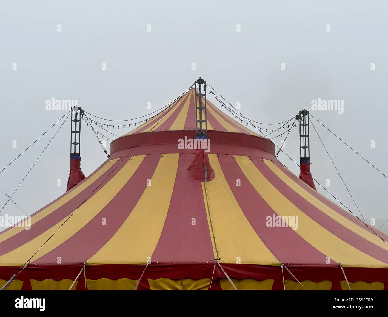Il tetto di una tenda da da circo a strisce rosse e gialle contro un cielo grigio nuvoloso Foto Stock