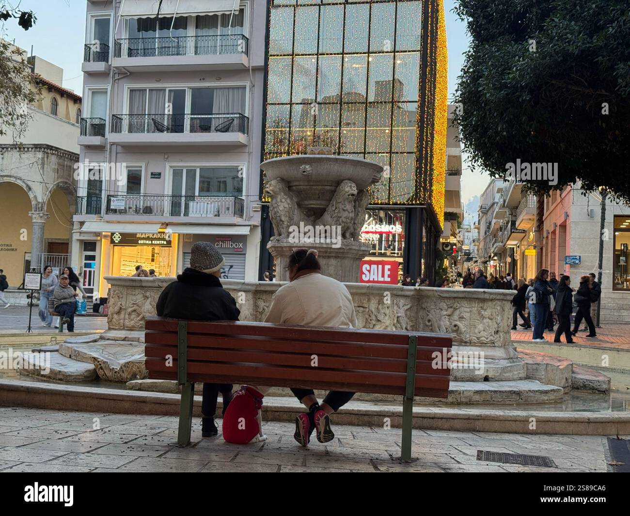 Due donne anziane con il loro cane siedono su una panchina di fronte alla fontana dei leoni o dei Morosini nella città di Heraklion durante la stagione invernale Foto Stock