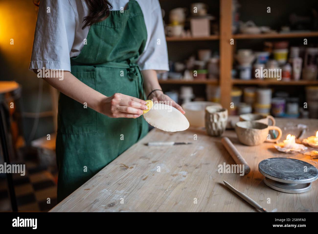 Donna artigiana con una forma a piattino in ceramica che dà forma alla spugna, per garantire la levigatezza dell'argilla in un laboratorio di ceramica Foto Stock