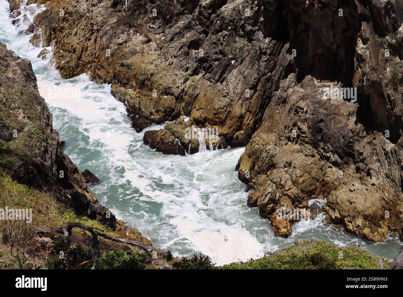 schiuma marina che riempie un canale stretto tra gli affioramenti rocciosi Foto Stock