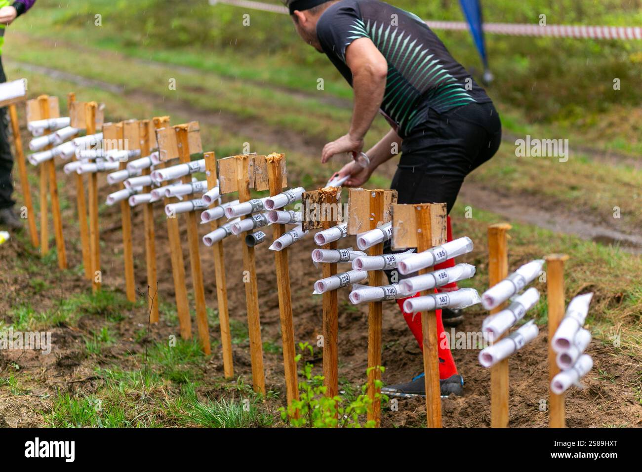 L'inizio del partecipante alla gara di orienteering nella staffetta durante la pioggia. Uomo che prende una mappa. L'area iniziale con le mappe della distanza Foto Stock