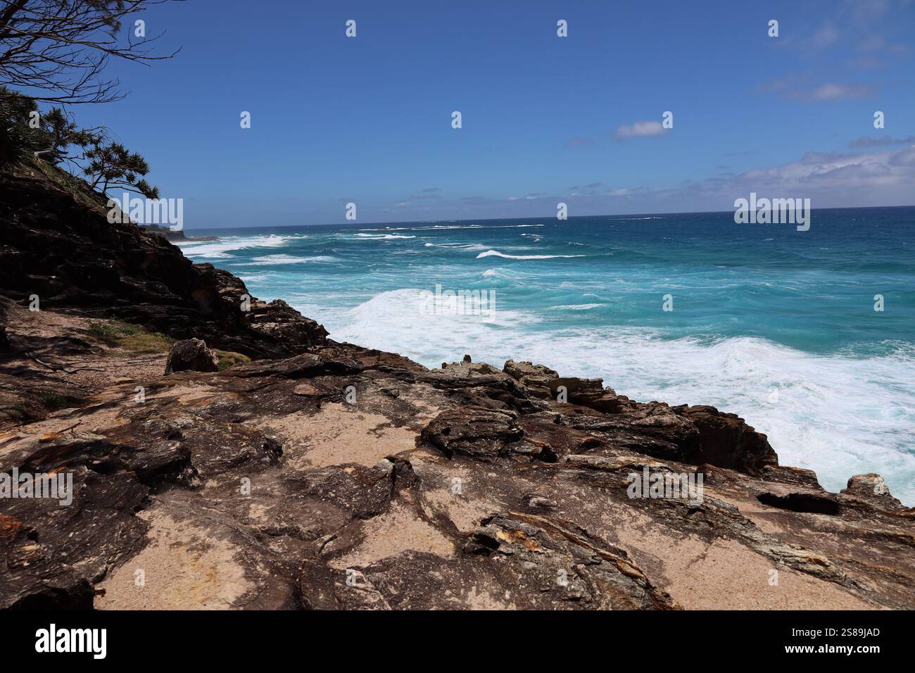 cieli azzurri, mari blu profondi, onde acquatiche e schiuma bianca lungo una costa rocciosa Foto Stock