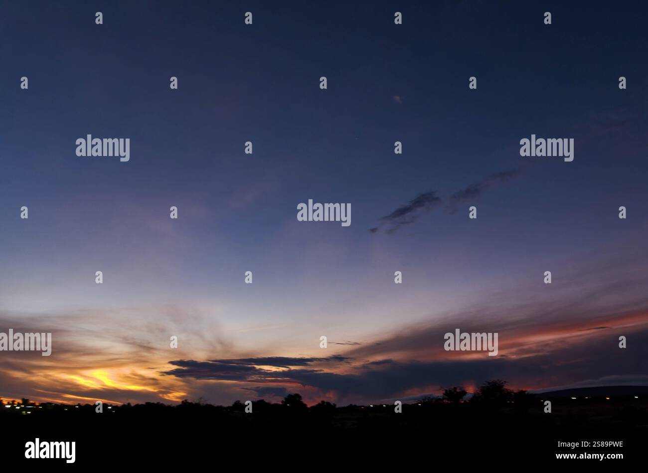 I colori caldi si fondono insieme nel cielo mentre il sole tramonta oltre l'orizzonte, trasformando il paesaggio in un ambiente pittoresco. Le nuvole catturano Foto Stock