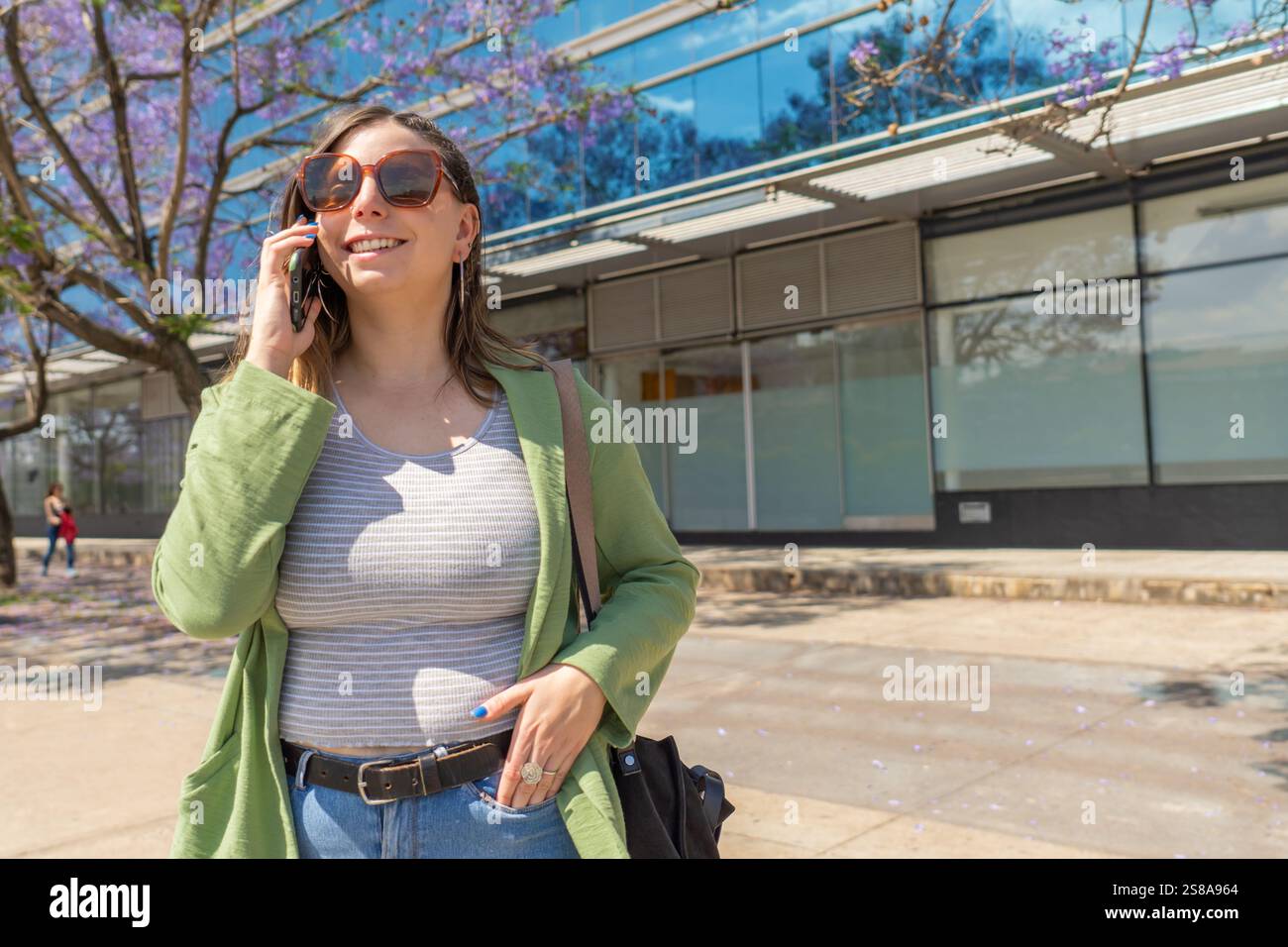 Giovane donna d'affari che parla al telefono mentre cammina in città durante il sole della primavera Foto Stock