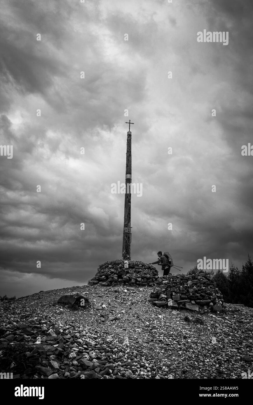 Pellegrino sul cammino di Santiago che offre pietre votive e offerte in Cruz de ferro (Croce di ferro), collina di Foncebadón, regione di Bierzo, Castiglia e León, Spagna. Foto Stock