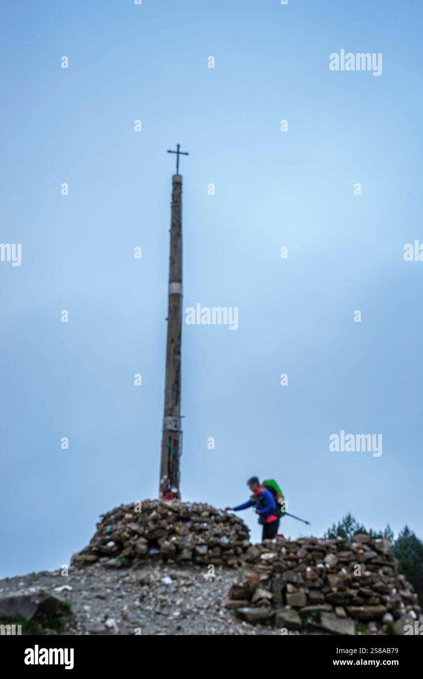 Pellegrino sul cammino di Santiago che offre pietre votive e offerte in Cruz de ferro (Croce di ferro), collina di Foncebadón, regione di Bierzo, Castiglia e León, Spagna. Foto Stock