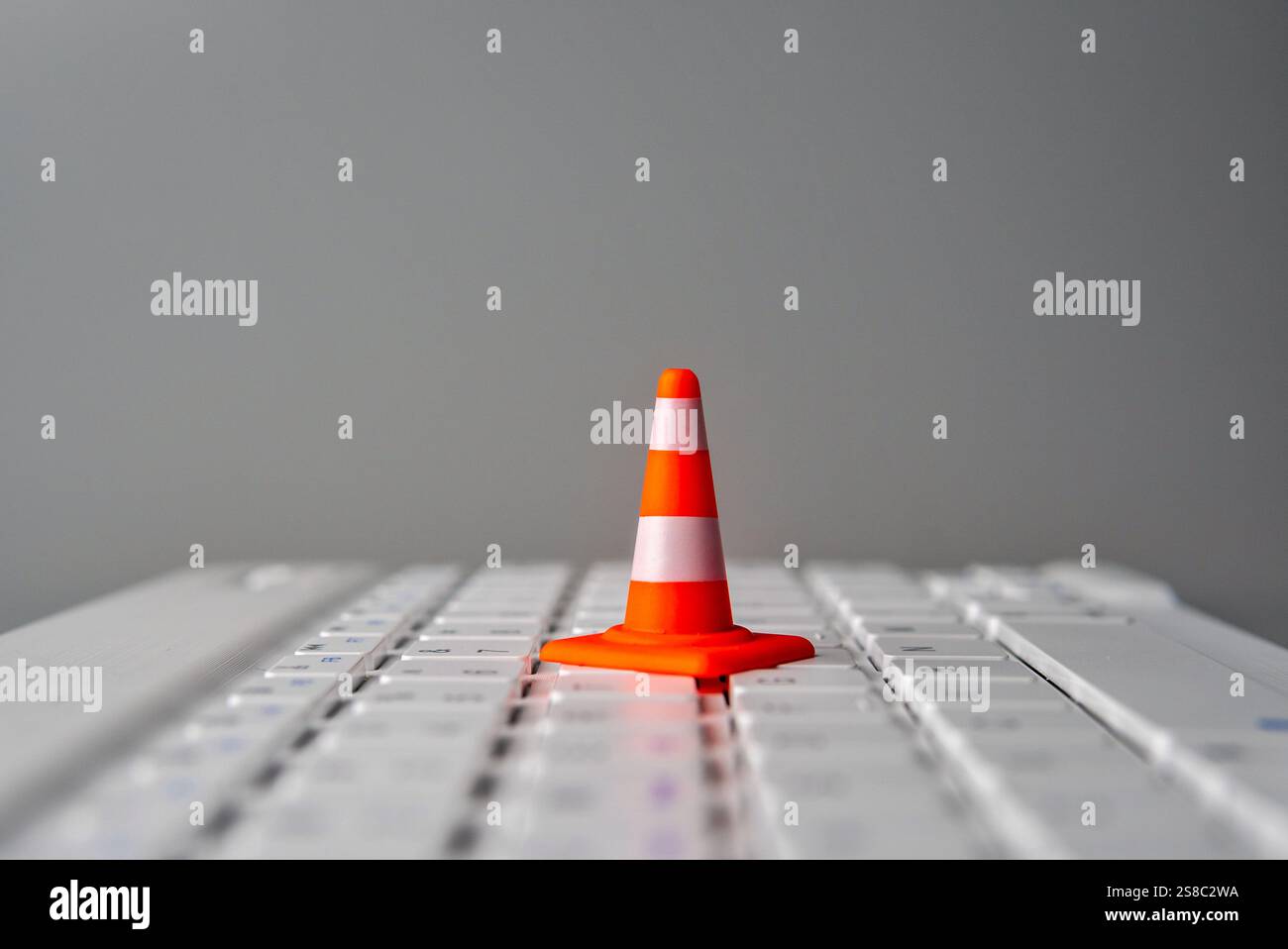 Un cono di traffico miniaturizzato su una tastiera di un notebook. Concetto di manutenzione del sito Web, tempi di inattività o difficoltà tecniche. Foto Stock