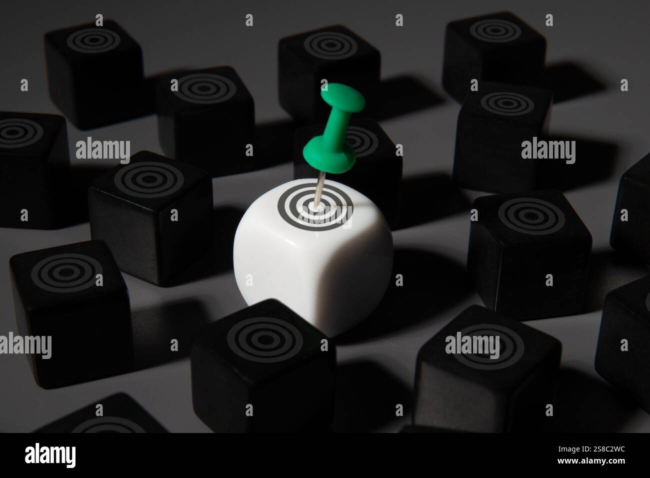 Un cubo bianco con un bersaglio e un puntale verde spicca tra i cubi neri. Definizione degli obiettivi, definizione degli obiettivi, concetto di concentrazione. Foto Stock