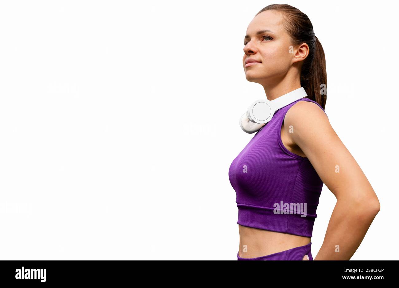 Una donna che indossa sport viola sta all'aperto con le cuffie sul collo isolate su sfondo bianco. Foto Stock