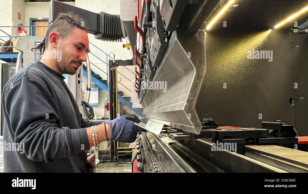 Giovane lavoratore che piega i metalli su un freno a pressione. Industria metallurgica Foto Stock