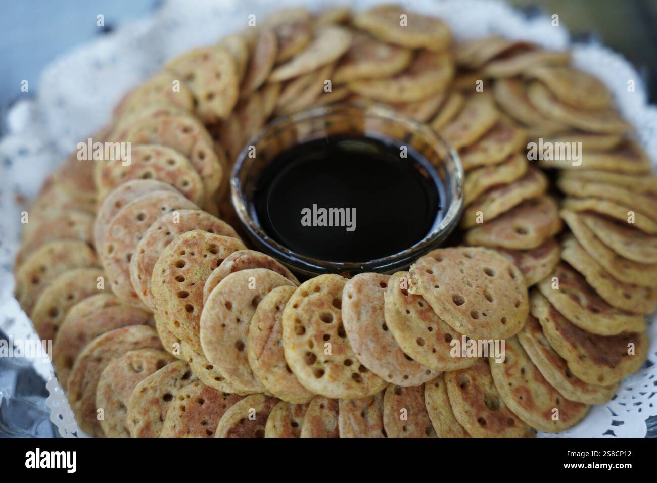 Un piatto splendidamente organizzato di mini pancake tradizionali serviti con una ciotola di ricco sciroppo di dattero. Perfetto per gustare la cucina culturale, durante le feste Foto Stock