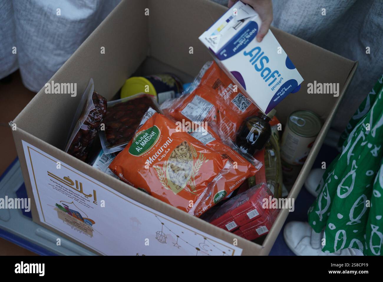 Scatola per donazione di alimenti contenente articoli essenziali come cartoni di latte, datteri confezionati, maccheroni e conserve. Rappresentazione perfetta di un charitabl Foto Stock