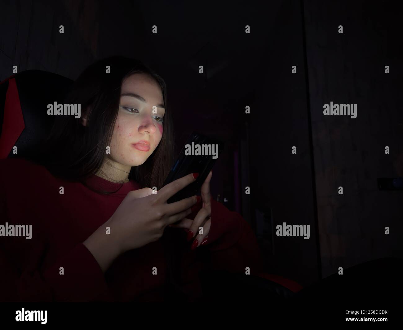 Giovane donna in una stanza buia illuminata dal bagliore dello schermo dello smartphone. Foto Stock