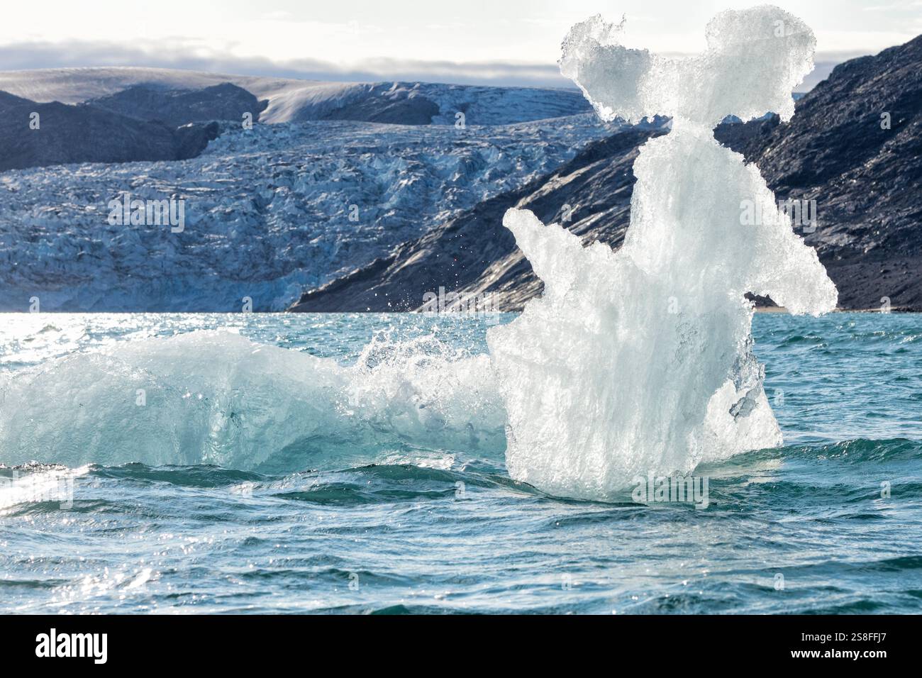 Un iceberg dall'aspetto divertente galleggia di fronte a un ghiacciaio che drena la calotta di ghiaccio groenlandese nella parte più interna del fiordo di Kangerlussuatsiaq Foto Stock