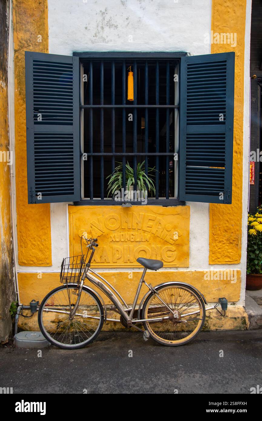 Una bicicletta si appoggia su una casa mercantile dipinta di giallo sotto una finestra con persiane d'epoca Foto Stock