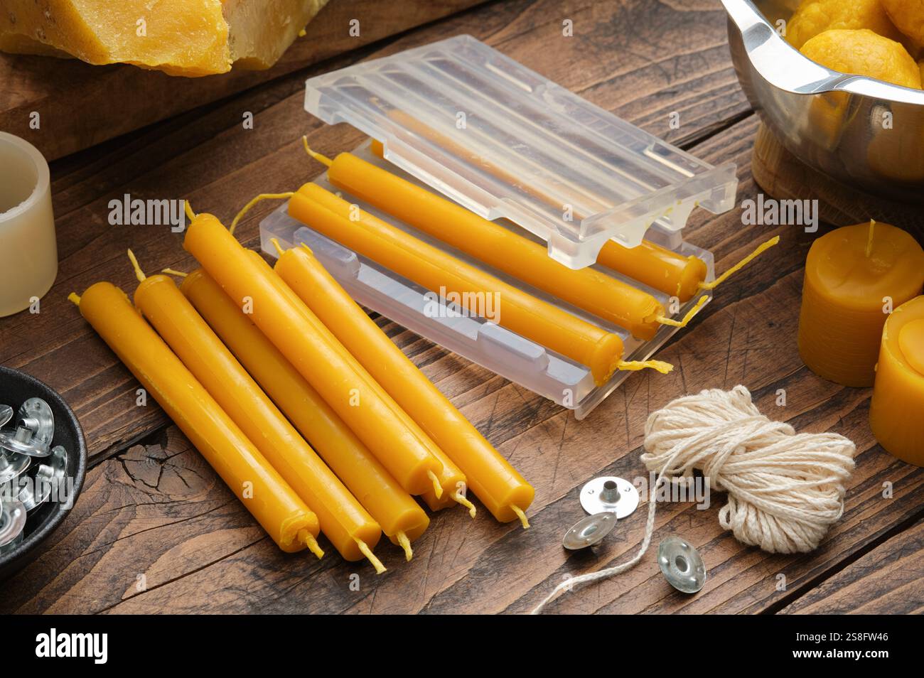 Cera d'api, stampi, stoppini, stoppini metallici, melting pot, coltello e utensili per realizzare candele naturali fatte a mano su una superficie in legno. Foto Stock