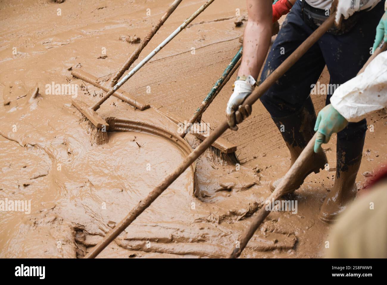 Volontari irriconoscibili con spazzole spazzatrici che spazzano fango e acqua sporca dalle strade dopo un disastro naturale. Foto Stock