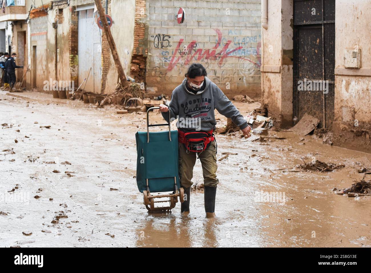 Uomo che cammina nel fango in una strada fangosa con un carrello dopo un disastro naturale. Massanassa, Spagna Foto Stock