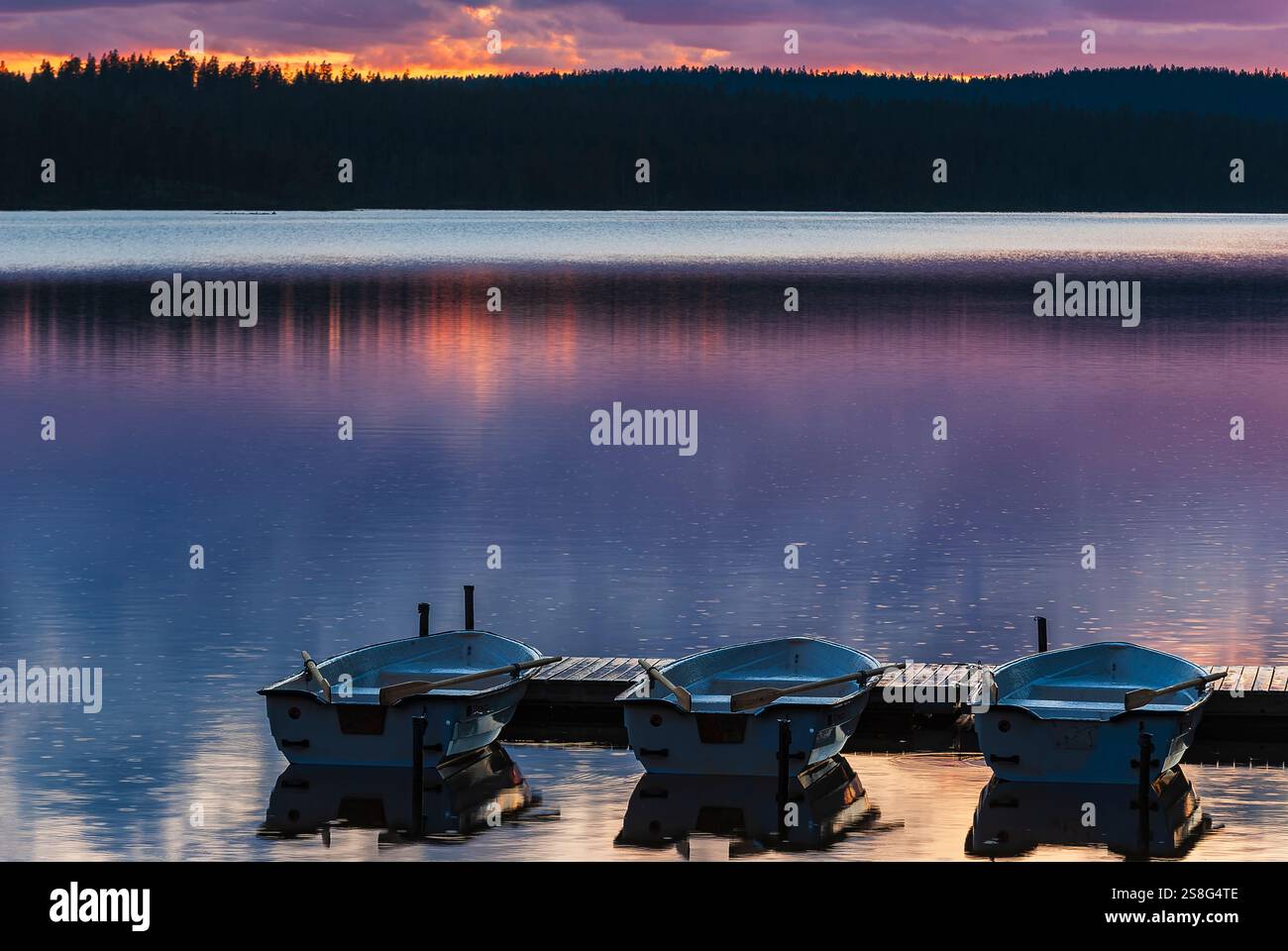 Le barche a remi sono legate a un molo, che rimbalza dolcemente sulle calme acque del lago Burusjon. I colori vibranti del tramonto si riflettono magnificamente sulla superficie, cre Foto Stock