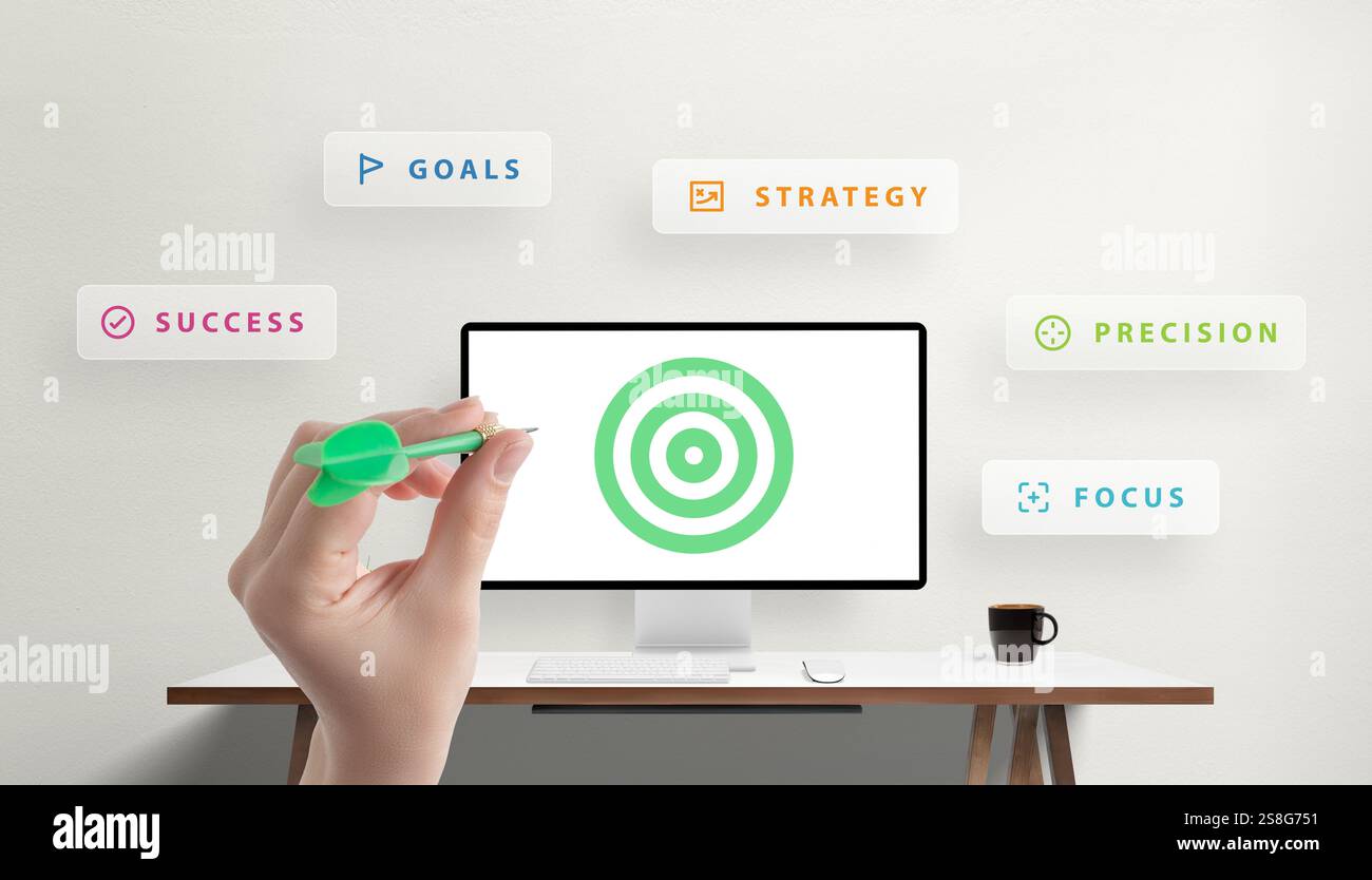 Mano che tiene in mano un dardo che mira a un bersaglio visualizzato su un monitor desktop, circondato da parole come obiettivi, strategia e successo, che simboleggiano la fusione o Foto Stock