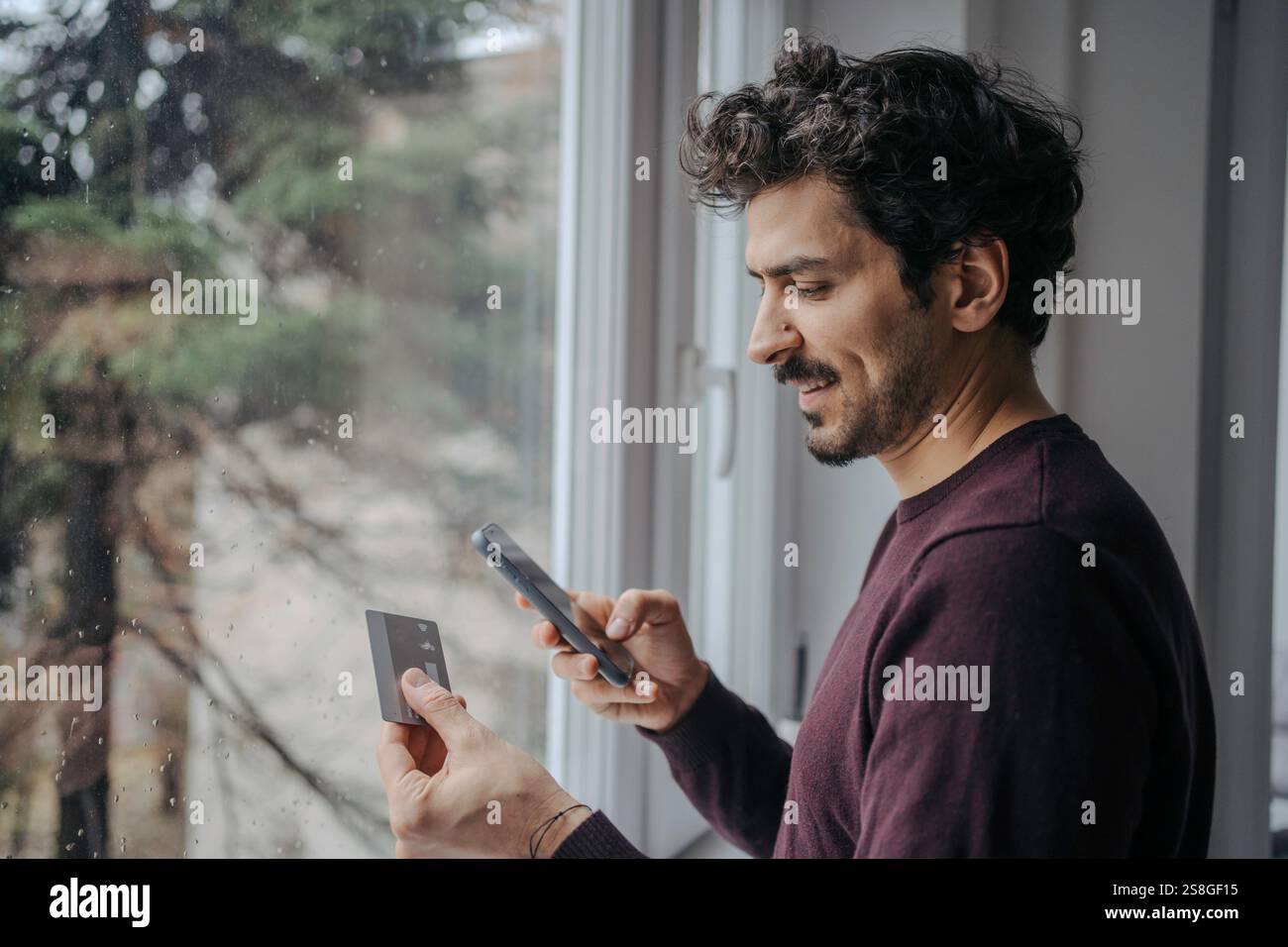 Giovane bel mediorientale che usa il telefono e la carta di credito e sorride. card e-banking online shop e-commerce Foto Stock