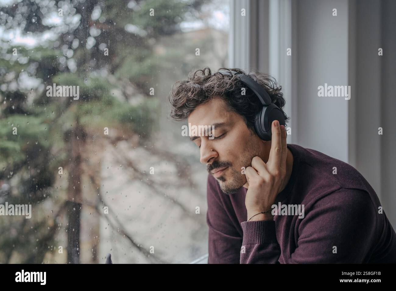 Giovane e affascinante uomo dall'aspetto mediorientale con cuffie sovraurali che ascoltano musica e si rilassano. Foto Stock