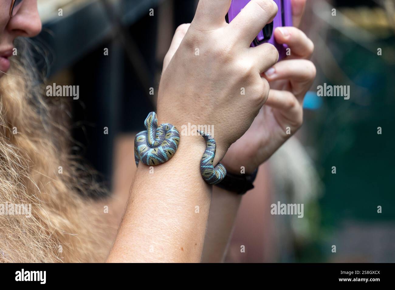 Donna che scatta un selfie tenendo un serpente colorato sul braccio in un giardino tropicale durante le ore diurne Foto Stock