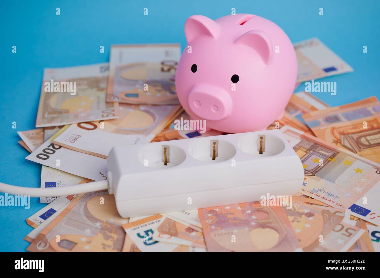 Un salvadanaio siede su una pila di banconote in euro accanto a una striscia di energia, simboleggiando la spesa energetica. Foto Stock
